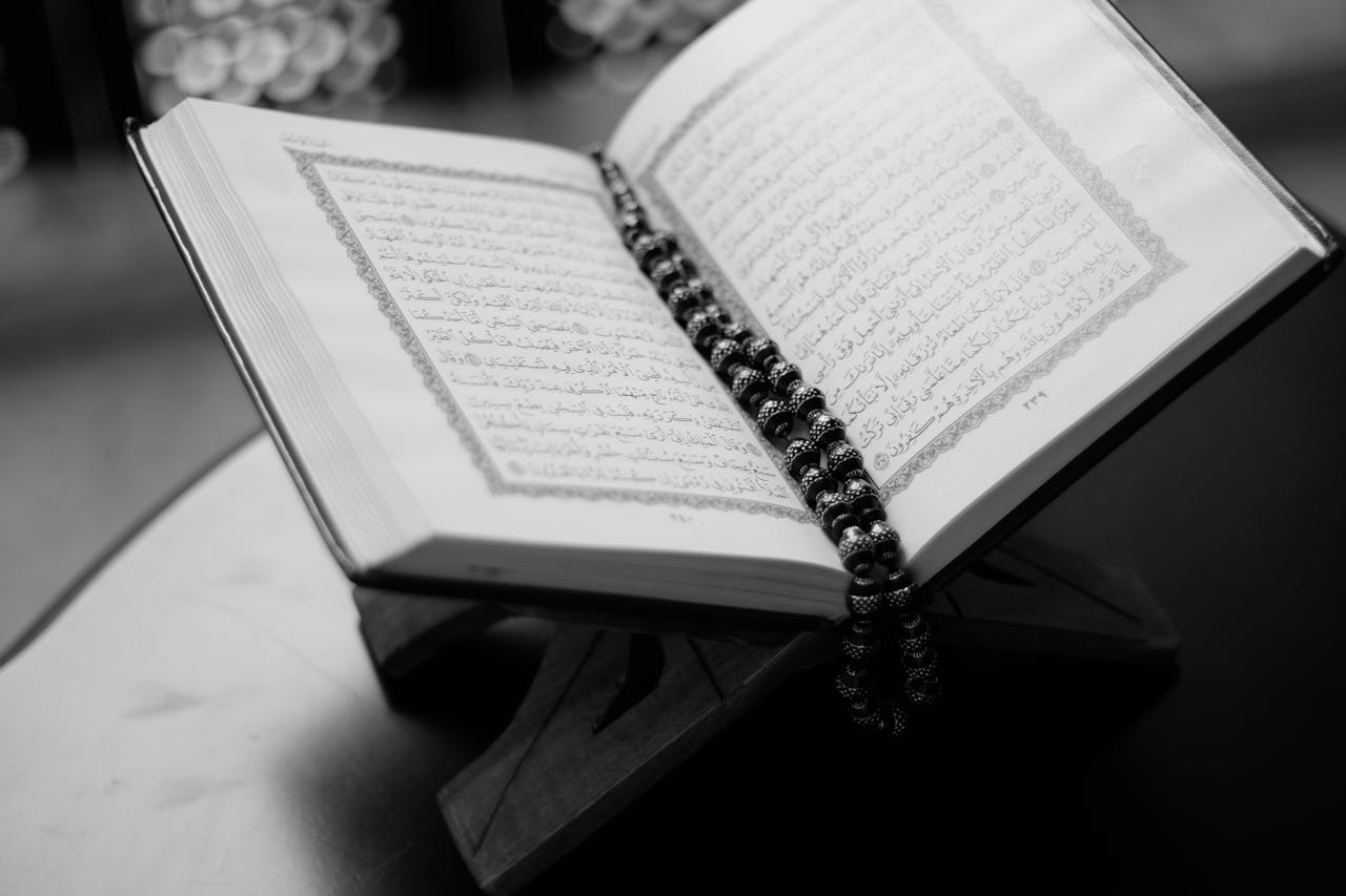 Crafting Captivating Headlines: Your awesome post title goes here A black and white close-up of an open Quran on a wooden stand with prayer beads, symbolizing Islamic faith and devotion.